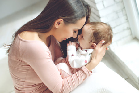 A loving mother caring for her newborn baby at home. Bright portrait of a happy mother holding a sleeping baby in her arms. High quality photo.の写真素材