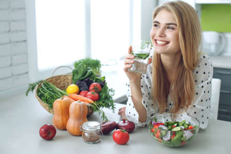 Woman on a diet. Young and happy woman eating healthy salad sitting on the table with green fresh ingredients indoors. High quality photoの写真素材