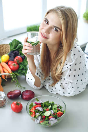 Woman on a diet. Young and happy woman eating healthy salad sitting on the table with green fresh ingredients indoors. High quality photoの写真素材