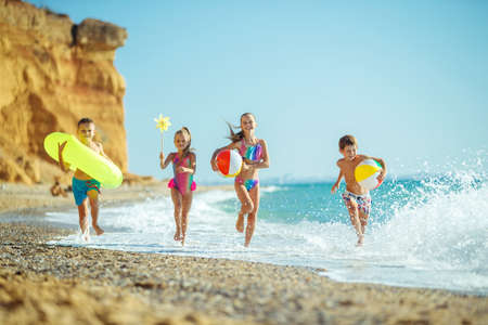 A group of children have fun playing at the sea. Children in bathing suits. Friends holding hands and running on the beach. High quality photo.の写真素材