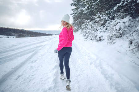 A woman runs in the snow in the winter mountains. Sports, fitness - inspiration and motivation. Woman jogging outdoors. High quality photo.の写真素材