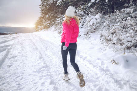 A woman runs in the snow in the winter mountains. Sports, fitness - inspiration and motivation. Woman jogging outdoors. High quality photo.の写真素材