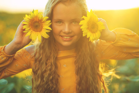 Beauty joyful girl with sunflower enjoying nature and laughing at summer sunflower field. Sun glare,...