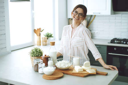 Young woman with milk, cottage cheese, sour cream, cheese in the kitchen at home indoors, beautiful girl sitting at the table, happy woman smile, natural organic. High quality photo.の写真素材