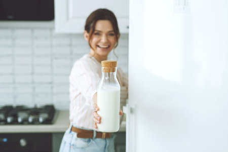 Young woman with milk in the kitchen at home indoors, beautiful girl sitting at the table, happy woman smile, natural organic. High quality photo.の写真素材
