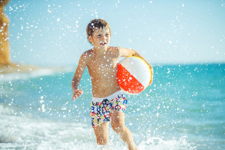 Boy child has fun at sea. Summer, happiness, sea and a child with a ball. High quality photo.
