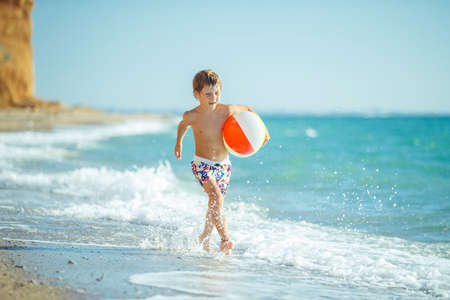 Boy child has fun at sea. Summer, happiness, sea and a child with a ball. High quality photo.の写真素材