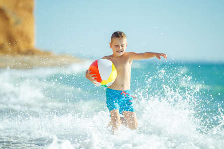 Boy child has fun at sea. Summer, happiness, sea and a child with a ball. High quality photo.の写真素材