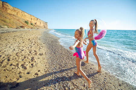 Children are playing on the beach. Children swim and play in the sea on summer family vacations. Sand and water activities. Two girls run on the ocean shore. High quality photo.の写真素材