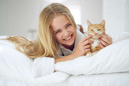 The girl is resting on the bed with her ginger kitten. A child with an animal. High quality photo.の写真素材