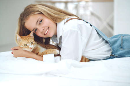 The girl is resting on the bed with her ginger kitten. A child with an animal. High quality photo.の写真素材