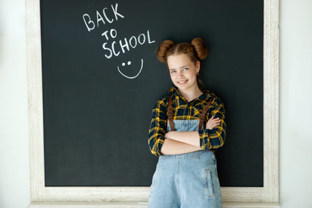 Happy smiling girl. Child at the blackboard. Girl indoor classroom with chalkboard on background. We...