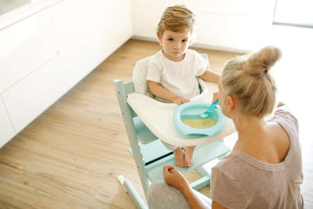 Mom feeds the baby. Young woman feeds her baby from a spoon at home. High quality photo.の写真素材