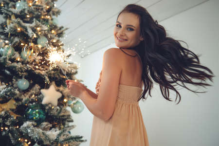 Young beautiful woman near the Christmas tree. Fashion beautiful sensual new year woman with makeup in a luxurious interior. High quality photoの写真素材