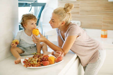 Mom feeds the baby. Young woman feeds her baby in the kitchen. High quality photoの写真素材