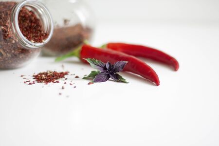 Spices in glass jars and powder pile, hot red pepper and basil leaves on white backgroundの写真素材