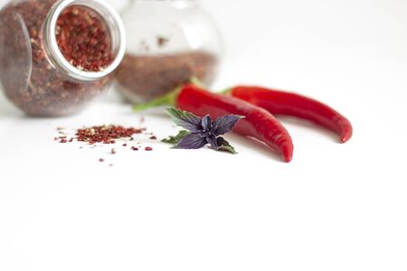 Spices in glass jars and powder pile, hot red pepper and basil leaves on white backgroundの写真素材