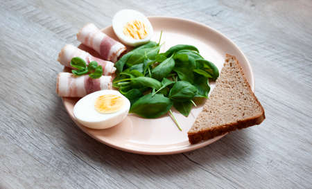 Food for breakfast. Plate with spinach leaves, green basil, bacon, eggs and a piece of rye bread. selective focusの写真素材