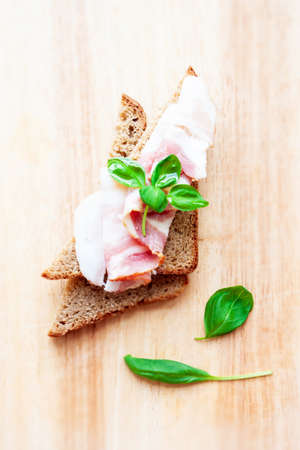 food. Sandwiches. Rye bread with bacon slice and basil leaf on wooden backgroundの写真素材
