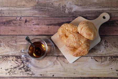 top view of a cup of tea and croissant on a wooden tableの写真素材
