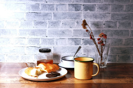 picture of foods in kichen bar, croissant, crackers, honey bottle, coffee cup and milk mug on wooden table as brick wall behindの写真素材