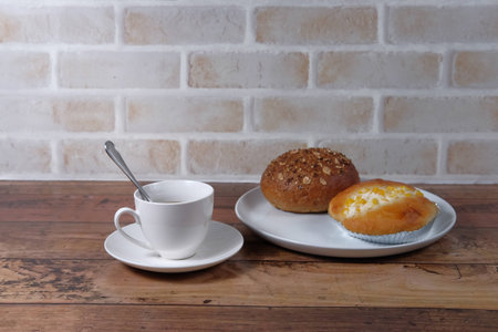 Picture of coffee and bakeries are on the wooden table in front of brick wallの写真素材