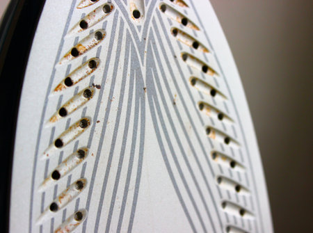 Detailed macro of a steam iron soleplate showing limescale and rust around steam holes. Cleaning, descaling, and maintenance concept.の写真素材