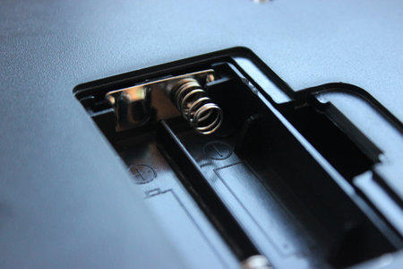 Vacant battery tray in macro detail shows shiny springs and contacts with plus and minus signs....