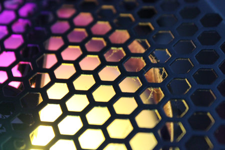 Vivid RGB light glows behind a hexagonal mesh inside a desktop case. Bright gradients and texture suggest gaming rigs, airflow, and PC hardware themes.の写真素材