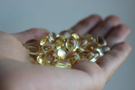 Human hand full of glossy golden fish-oil softgels, omega-3 nutrition and supplement concept, macro...