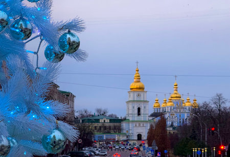 Golden Domes Cathedral in Kyiv with Christmas tree and evening traffic. Urban winter holiday scene with decorated fir branch and city lights in soft blue tones.の写真素材