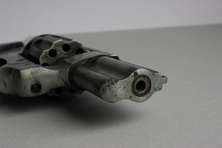 Close-up macro of a worn revolver barrel lying on a white background. Industrial, gritty texture and...