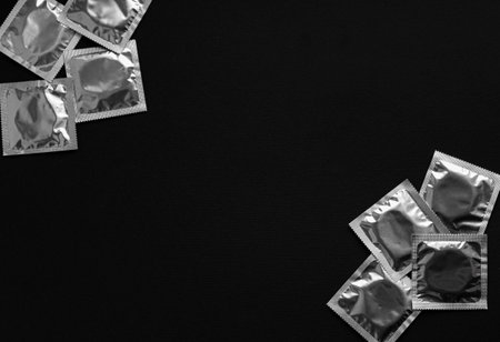 Silver condom packets arranged in two groups on a black background, leaving wide copy space in the...