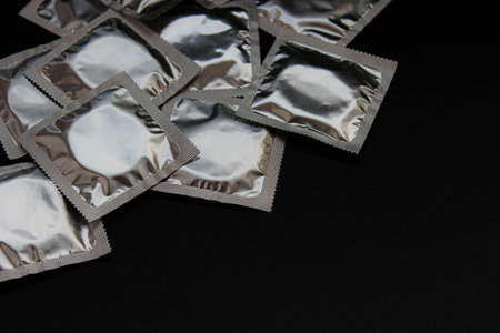 Wide arrangement of multiple foil-wrapped condoms on a black background. High-contrast product scene, no brands, safe-sex message.の写真素材