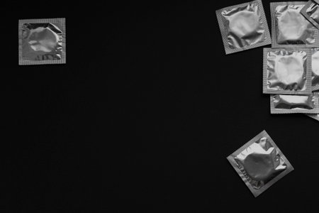 One foil condom packet isolated with a cluster at right on a black background. Ample copy space for safe-sex or awareness campaign designs.の写真素材