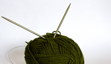 Close-up of a dark olive yarn ball with two circular metal knitting needles, clean white backdrop...