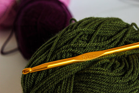 Shiny gold 6.0 mm crochet hook placed across a dark green skein with colorful balls in soft bokeh....
