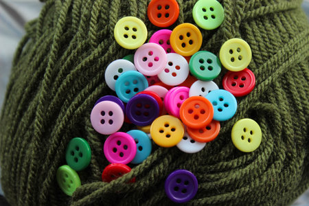 Bright four-hole plastic buttons scattered over green yarn. Close macro with shallow depth of field...