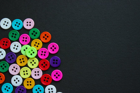 Dense cluster of bright sewing buttons in one corner against black paper, leaving generous copy space.の写真素材