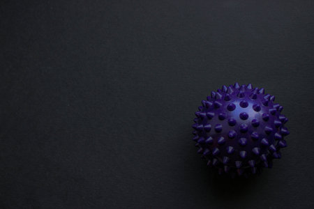 Purple spiky massage ball isolated on a dark textured background with wide copy space. Minimal product shot for fitness, rehab, and wellness themes.の写真素材