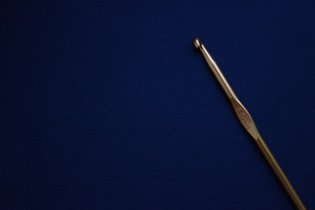 Golden 6.0 mm crochet hook placed diagonally on a dark blue textile background with plenty of copy space.の写真素材