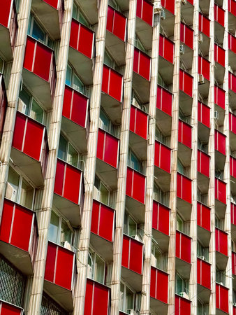 Residential high-rise with repeating red balcony panels and vertical concrete fins, urban...