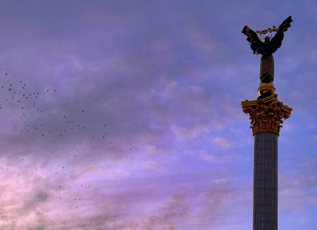 Close view of the Independence Monuments angel statue framed by soft purple clouds and a flock of...