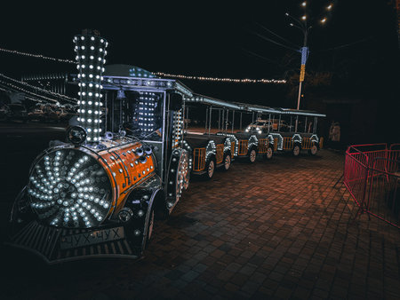 A brightly lit festive train stands parked at night, glowing with green and yellow lights. holiday...