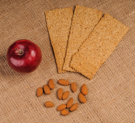 Red apple with crispbread and almonds on sacking backgroundの写真素材