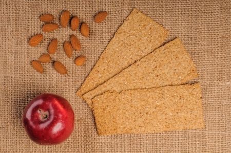 Red apple with crispbread and almonds on sacking backgroundの写真素材