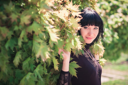 Young woman standing near a maple with lush foliageの写真素材