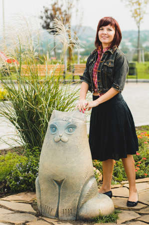 Young woman standing near funny cat statue in summer dayの写真素材