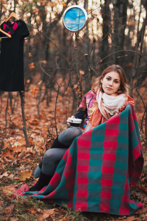 Beautiful girl sitting on armchair in autumn forest with cup in her handsの写真素材