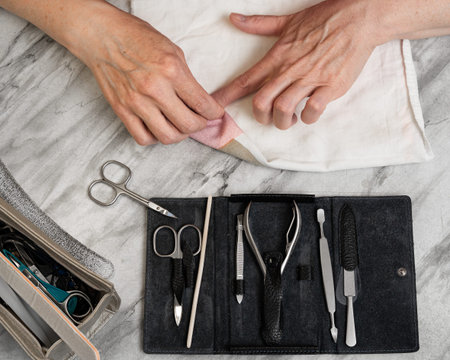 A woman aged 47-48 makes herself a manicure, takes care of her nails and fingers at the table at home. Prepares nails and fingers for processing top view close-upの写真素材